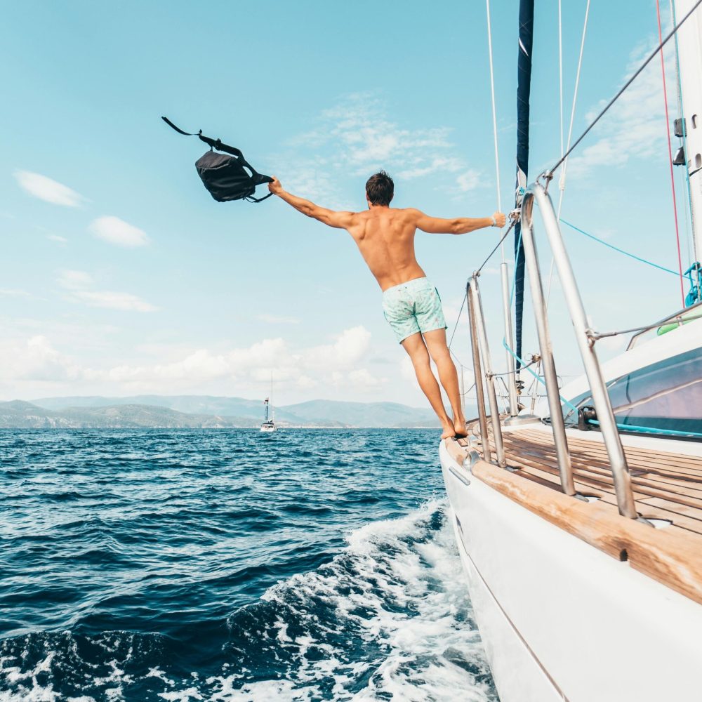 Man enjoying freedom by jumping into the ocean from a sailboat in Greece.