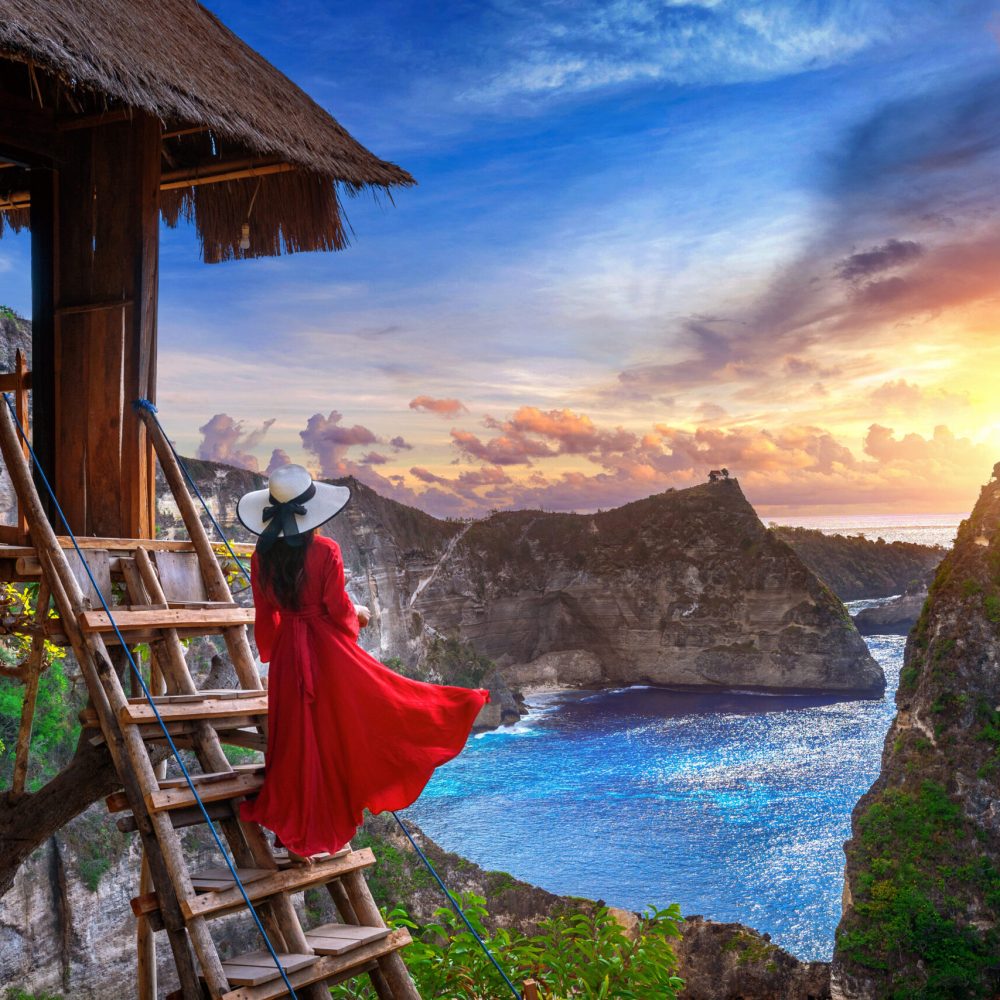 Young girl on steps of house on tree at sunrise in Nusa Penida island, Bali in Indonesia.